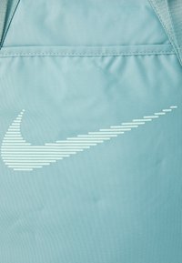 Lichtblauwe stof met horizontale witte strepen en het Nike swoosh logo, met zichtbare stiknaad aan de bovenrand.
