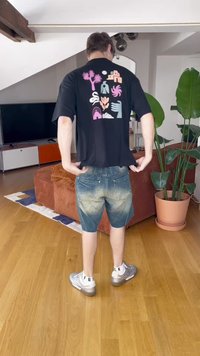 T-shirt preta com designs gráficos coloridos nas costas, combinada com calções de ganga azuis com uma textura desbotada e bainha em contraste. Sapatos prateados.