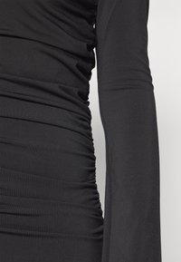 Μαύρο μακρυμάνικο φόρεμα με πτυχές στη μία πλευρά, λείες υφές και εφαρμοστό σχέδιο.