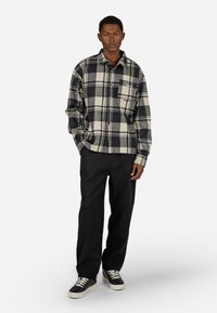 Fekete és krémszínű kockás flaneling hosszú ujjakkal, gombos elülső résszel, mellzsebbel és laza szabással, fekete nadrággal és sportcipővel párosítva.