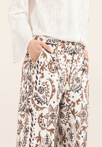 Pantaloni in lino con una base bianca e motivi floreali marroni e neri, design svasato, tasche laterali e una parte anteriore plissettata.