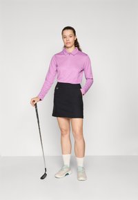 Lilla langermet polo med glidelås i kragen, parret med et svart miniskjørt. Hvite sokker og lysegrå golfsko med turkise detaljer.