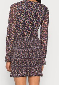 Květinové šaty s černým podkladem, zdobené drobnými barevnými květy. Dlouhé průsvitné rukávy, řasený pas a volánkový lem. Lehká tkanina.