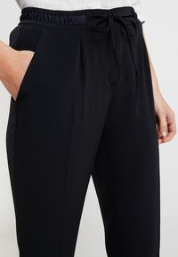 Svarta elastiska midjebyxor med snöre, med sidofickor och ett mjukt, lätt tyg, skräddarsydd passform och rena linjer.