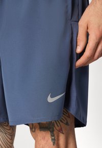 Nike sports shorts in navy blue, featuring a smooth texture, side mesh panel, and silver logo accent on the lower left.