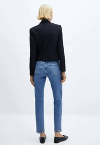 Blazer negro corto sobre jeans de mezclilla azul claro, con un diseño ajustado y detalles m�ínimos. El conjunto se completa con bailarinas negras.