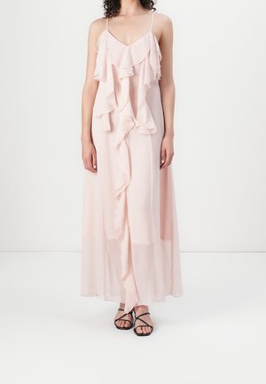 Dlouhé světle růžové šaty s volánkovými detaily, tenkými ramínky a vzdušnou texturou. Kombinované s černými sandály na tenkých páscích.