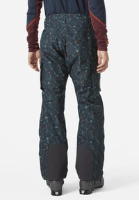 Skibroek in diep teal met een meerkleurig spikkelpatroon. Voorzien van verstevigde zwarte manchetten en cargozakken aan de zijkanten. Waterdicht materiaal.