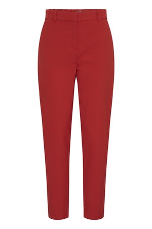 Nærbillede af person iført skræddersyede røde bukser med hænderne i lommerne og en hvid skjorte med lange ærmer stoppet ind.