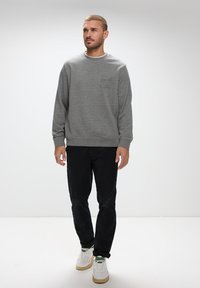 Grå sweatshirt med rund hals, ribbade ärmslut och nederkant. Mörka byxor och vita sneakers med gröna detaljer. Enkel design, inga mönster.