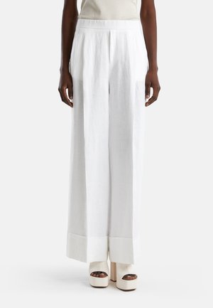 Pantalones de lino blancos de pierna ancha con pliegues delanteros y dobladillos acampanados, combinados con zapatos de plataforma gruesos. Textura suave, corte holgado.