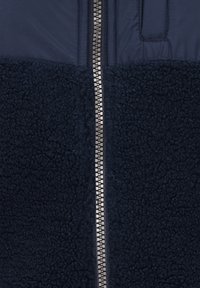 Chaqueta azul marino con la mitad inferior de forro polar texturizado y la parte superior de tela suave, con un cierre central de cremallera y dientes metálicos.