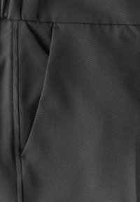 Schwarzer Stoff mit einer glatten Textur, der eine Seitentasche und subtile Nähte aufweist. Das Material wirkt leicht und strapazierfähig.