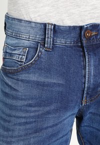Jeans in denim di un blu medio, con una vestibilità classica, dettagli sbiaditi, una tasca frontale e chiusura con bottone metallico.