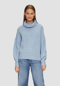 Hellblau gestrickter Pullover mit Kapuze, lockerer Passform und geripptem Textur. Kombiniert mit hellblauen Jeans.