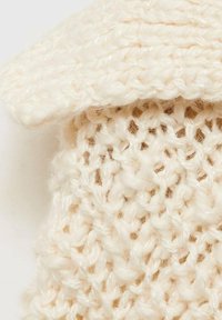 Stickad krämfärgad mössa med ribbad textur, med en vikt bräm och lösa stygn för ett mjukt utseende.