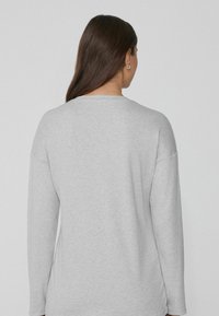 Top de manga larga gris claro, hecho de una tela suave, con un clásico escote redondo y costuras de hombros caídas para un ajuste relajado.