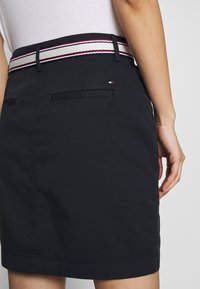 Marineblauwe rok met een contrasterende tailleband met rode en witte strepen. Voorzien van achterzakken en een rechte snit bij de zoom.