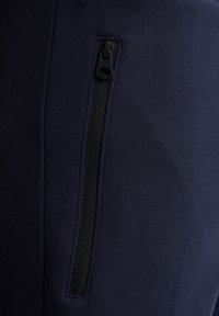 Navyblauwe stof met een gladde textuur, voorzien van een zwarte ritszak. Het ontwerp bevat gestikte naden voor duurzaamheid.