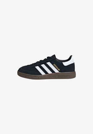 Baskets Adidas Spezial noires avec des bandes blanches, un œillet blanc au talon, une semelle marron et un marquage doré "Spezial" sur le côté.