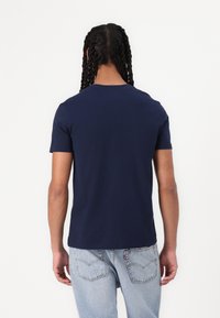 Marineblå kortermet t-skjorte laget av glatt stoff, med rund hals. Brukt sammen med lyseblå jeans som har et minimalistisk design.