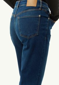 Dunkelblaue Jeans aus Denim mit enger Passform, ausgestattet mit einem braunen Lederetikett am Bund und sichtbaren Gesäßtaschen mit gesteppten Akzenten.