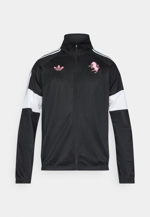 Black zip-up track jacket with white and pink accents. Features Adidas logo and Ferrari horse emblem, made from a smooth, lightweight fabric.