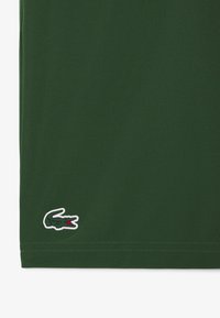 Camiseta de algodón verde con un logo de cocodrilo bordeado en blanco en el dobladillo. Textura suave, mangas cortas y un diseño de corte recto.