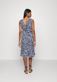 Vestido padrão azul-marinho e branco com alças franzidas, costas em V e bainha rodada, feito de um tecido texturizado e com uma cintura ajustada.