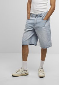 Shorts en denim bleu clair avec une coupe décontractée, dotés de poches latérales, d'une fermeture à bouton et d'un ourlet plié au niveau du genou.