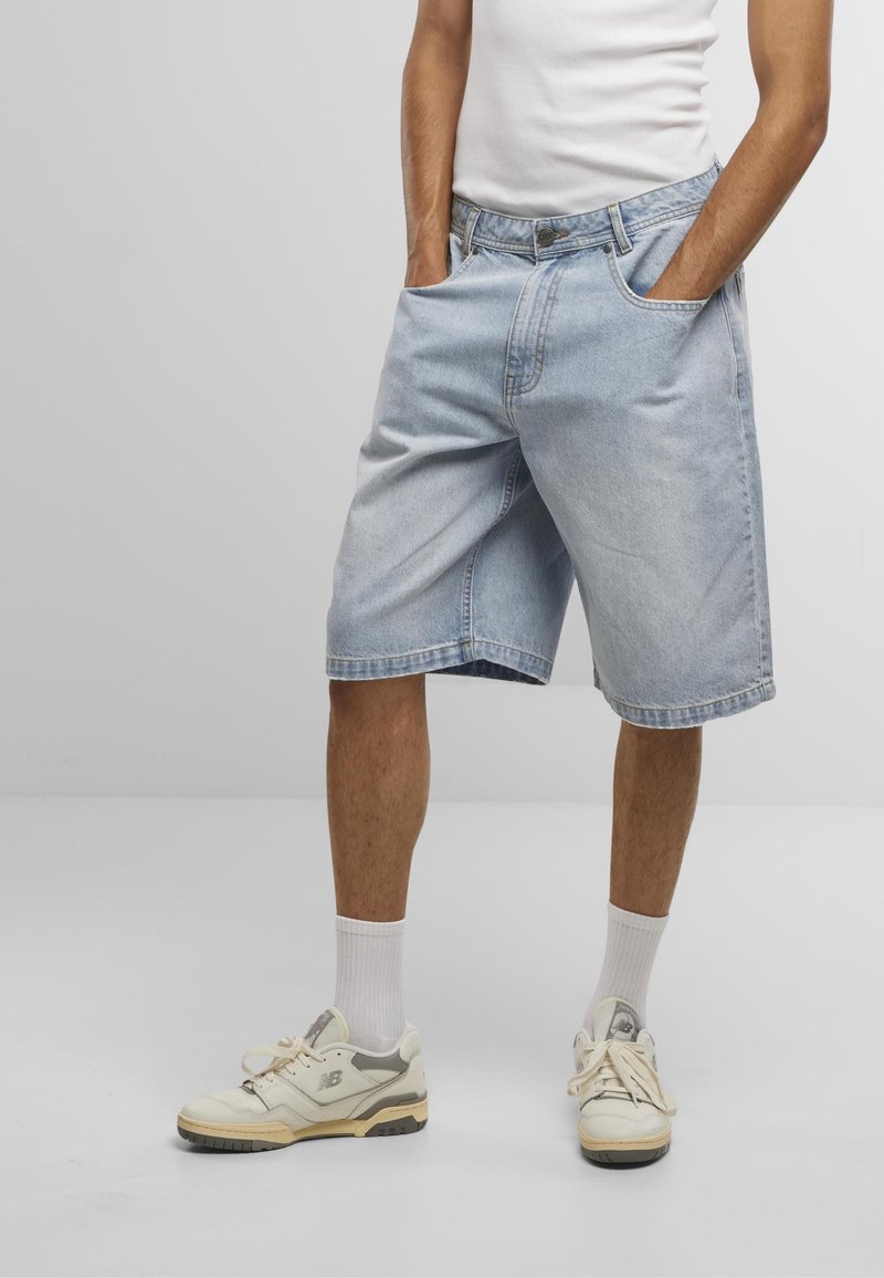 Shorts en denim bleu clair avec une coupe décontractée, dotés de poches latérales, d'une fermeture à bouton et d'un ourlet plié au niveau du genou.
