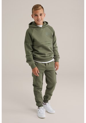 Set di felpa e pantaloni jogger verde oliva, con un logo sul petto, dettagli a coste e tasche cargo, abbinato a sneakers bianche.