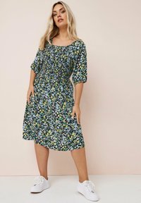 Blumenkleid mit schwarzem Hintergrund, Kurzarm Puffärmeln, quadratischer Ausschnitt und tailliertem Schnitt, kombiniert mit weißen Sneakers.