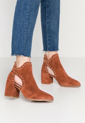 Brown suede ankle boots with cut-out sides and stud detailing worn with blue cropped jeans.