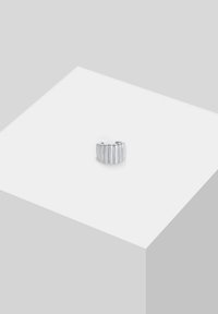 Silberring mit einem strukturierten, gerippten Design, das einen Halbkreis bildet. Seine glatte Oberfläche steht im Kontrast zu ausgeprägten Linienmustern.