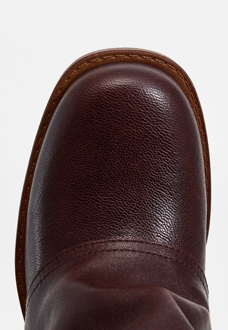 Botte en cuir marron avec une finition texturée, bout arrondi et surpiqûres marron contrastantes le long de la semelle. Tige lisse sans matériel visible.