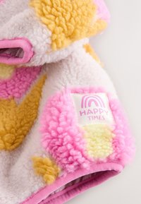 Couverture en polaire composée de patches jaunes, roses et blancs ; surface texturée avec une sensation de douceur ; comprend une étiquette portant l'inscription « HAPPY TIMES » avec un graphique arc-en-ciel.