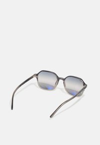 Óculos de sol com uma armação cinza, semi-translúcida e lentes degradê, apresentando uma forma geométrica e hastes alongadas.