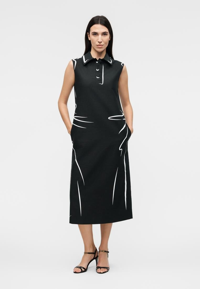 Femme portant une robe midi noire sans manches avec des motifs abstraits blancs en lignes, col boutonné, poches et talons noirs à brides, debout avec assurance.