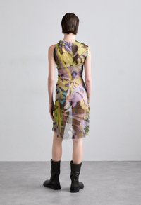 Robe transparente avec un imprimé botanique dans des teintes de jaune, vert et marron. Elle présente une coupe ajustée, un design sans manches et un détail de bouton à l'arrière.