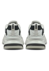 Białe i czarne sneakersy o masywnym designie, z teksturowaną tkaniną, wyściełanym kołnierzem i gumową podeszwą. Charakterystyczne logo na tyle buta.