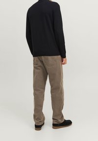 Svart stickad tröja, beige kordflöjtbyxor och svarta skor. Tröjan har långa ärmar och en rundad halsringning. Byxorna har bakfickor.