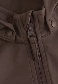 Brun utomhusjacka med en del som har dragkedja och knappar. Tyget har en slät yta med synlig sömnad längs sömmarna.