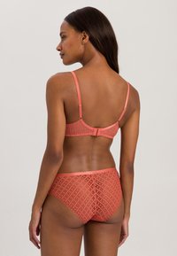 Koraal kleurig lingeriesetje met een geometrisch patroon, gekenmerkt door verstelbare bandjes, een haaksluiting en gegolfde kantafwerking aan de onderkant.