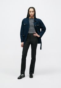 Veste marine à boutons dorés sur une chemise rayée noir et blanc, associée à un pantalon noir ajusté et des mocassins noirs. Textures de tissu lisses.