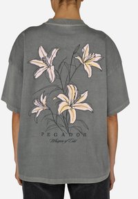 Üks suur hall puuvillane T-särk, mille eest on värvikas lilleprindiga roosa liiliate ja tekstiga "PEGADOR Whispers of Cold".
