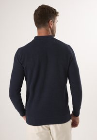 Marineblå strikket polo sweater med en tekstureret overflade, lange ærmer og en ribbet krave. Har et solidt bånd i kanten for et tætsiddende udseende.