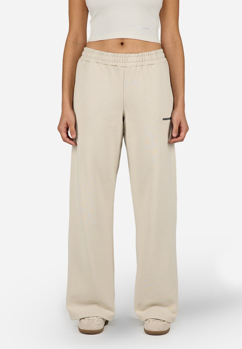 Bézs színű, bőszárú melegítőnadrág rugalmas derékpánttal és diszkrét márkajelzéssel az oldalon. Puha, sima tapintású anyagból készült.