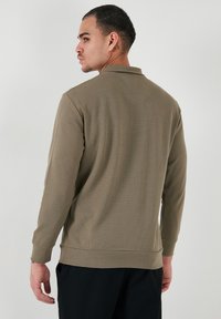 Polo majica dugih rukava u prigušenoj maslinastoj zelenoj boji. Ima teksturiranu tkaninu, rebrasti ovratnik i manšete. Casual kroj s ravnim porubom.