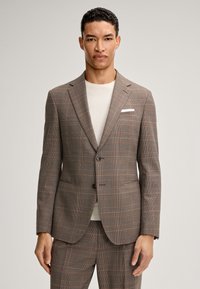 Brązowa marynarka w kratę wykonana z gładkiej tkaniny. Posiada zapięcie na dwa guziki, wyraziste klapy oraz kieszeń na piersi z białą chusteczką.